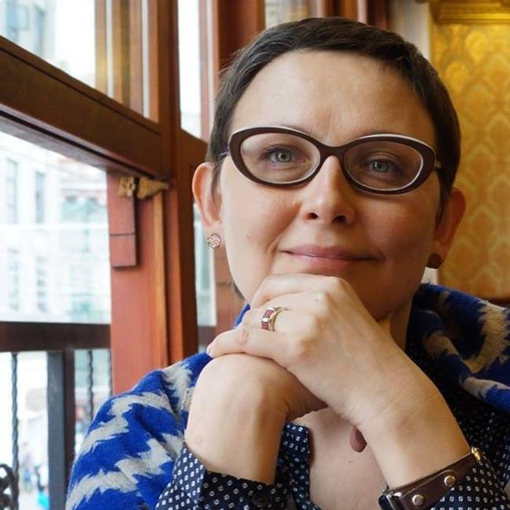 Die oppositionelle Künstlerin Olga Tsaplya Egorova. Sie trägt kurzes, dunkles Haar und eine Brille. Hier sitzt sie vor einem Fenster und stützt sich auf ihre Hände. 
