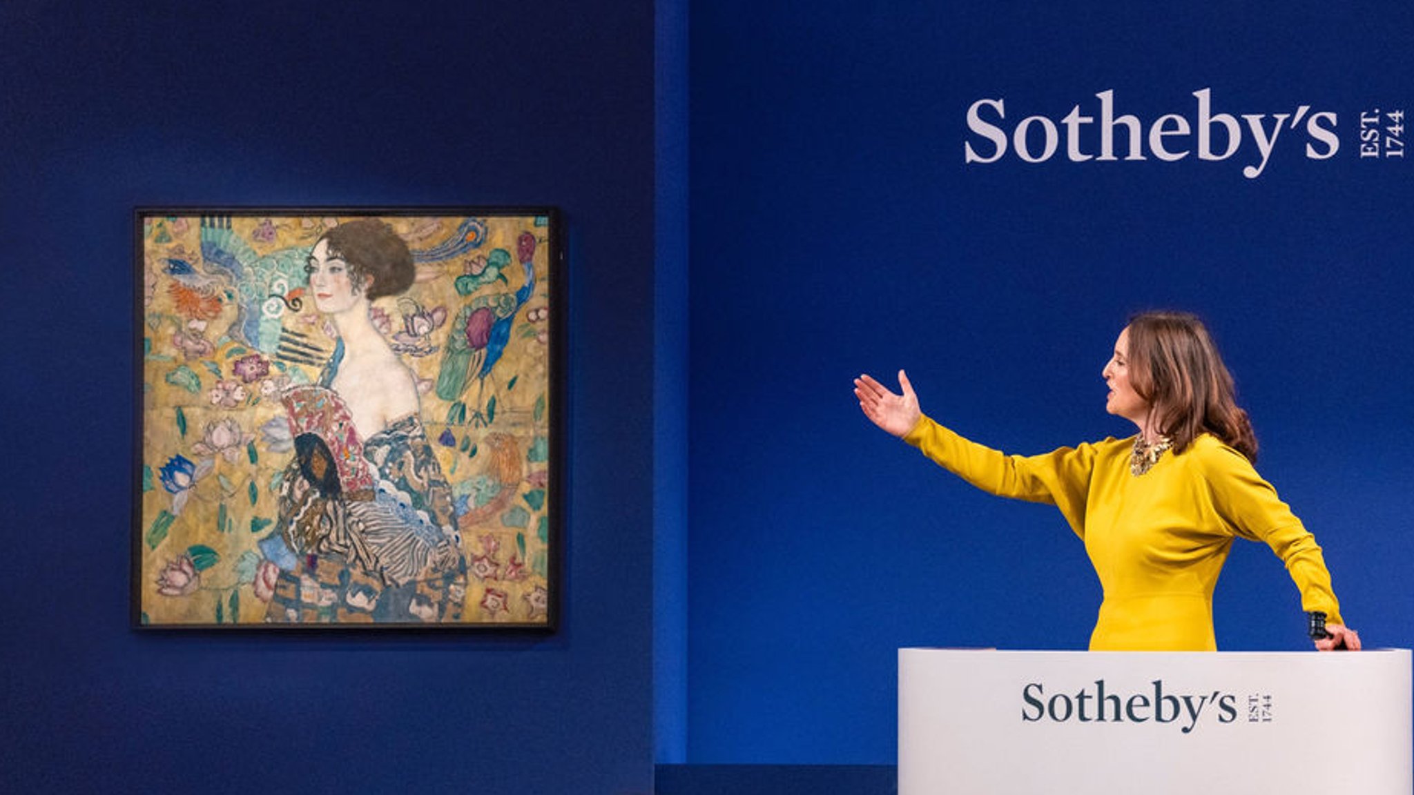 HANDOUT - 27.06.2023, Großbritannien, London: Die Auktionatorin Helena Newman zeigt bei der Auktion bei Sotheby's auf das Gemälde "Dame mit Fächer", das letzte Porträt des österreichischen Künstlers Gustav Klimt. Das Gemälde ist für 85,3 Millionen Pfund (99,2 Millionen Euro) versteigert worden und hat damit gleich mehrere Rekorde gebrochen. Wie das Auktionshaus Sotheby's am Abend mitteilte, ist noch nie bei einer Versteigerung in Europa so viel für ein Kunstwerk bezahlt worden. Foto: Haydon Perrior/Sotheby's/PA Media/dpa - ACHTUNG: Nur zur redaktionellen Verwendung im Zusammenhang mit der aktuellen Berichterstattung und nur mit vollständiger Nennung des vorstehenden Credits +++ dpa-Bildfunk +++