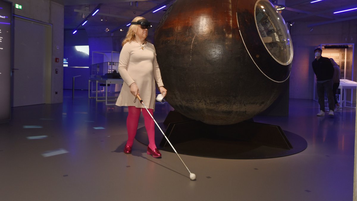 Eine Frau läuft mit VR-Brille und Blindenstock durchs Nürnberger Zukunftsmuseum.
