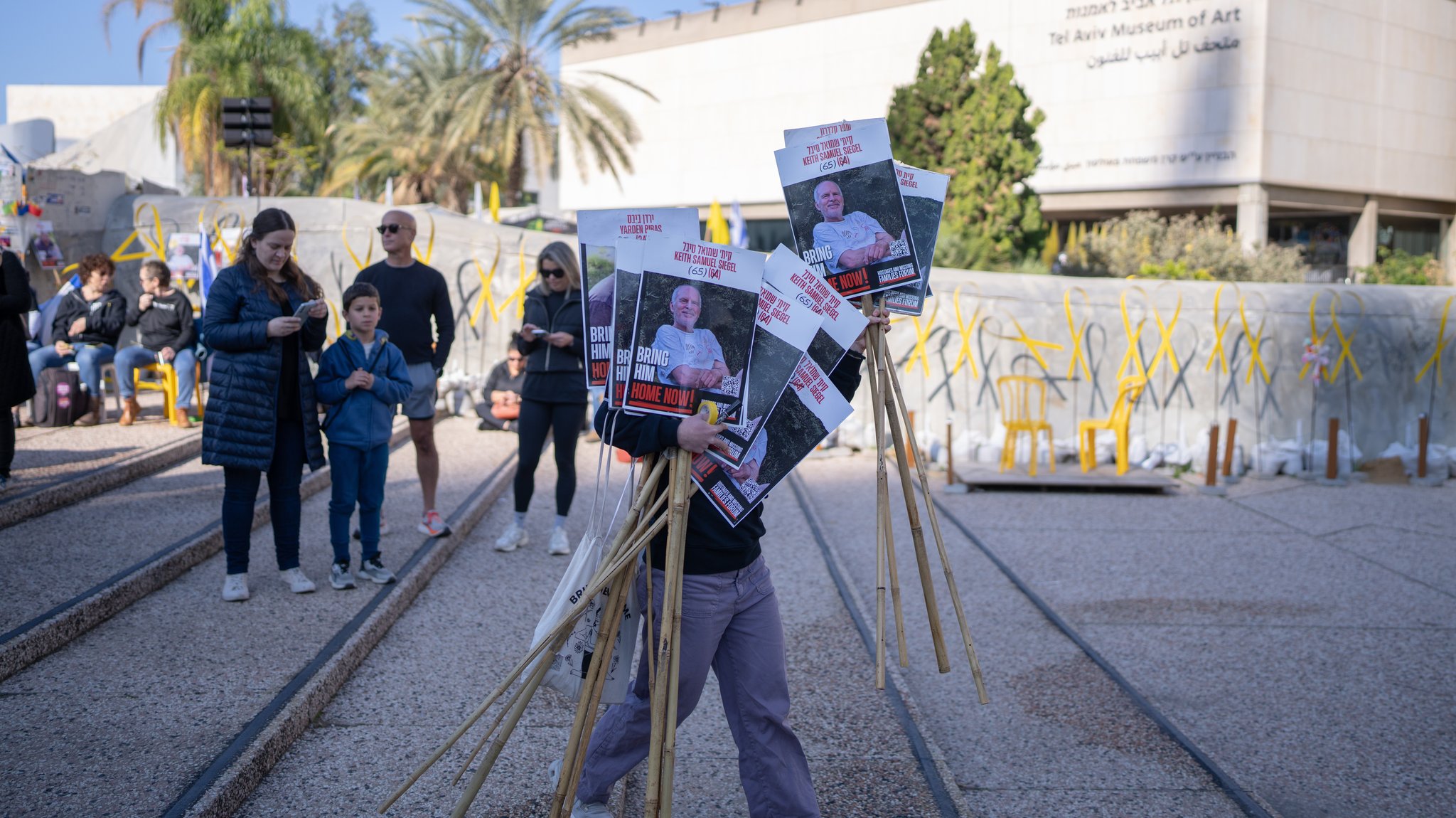 Ein Israeli hält Plakate von Geiseln, während er eine Live-Übertragung der Geiselübergabe verfolgt.