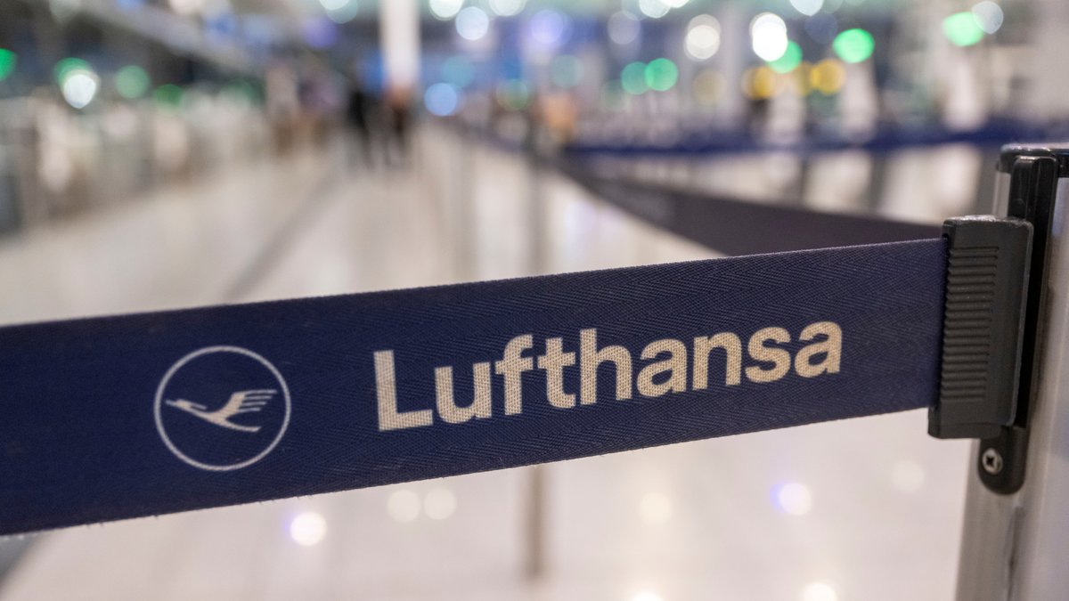 Das Logo der Lufthansa ist auf einem Absperrband am Check-in am Flughafen zu sehen (Symbolbild)