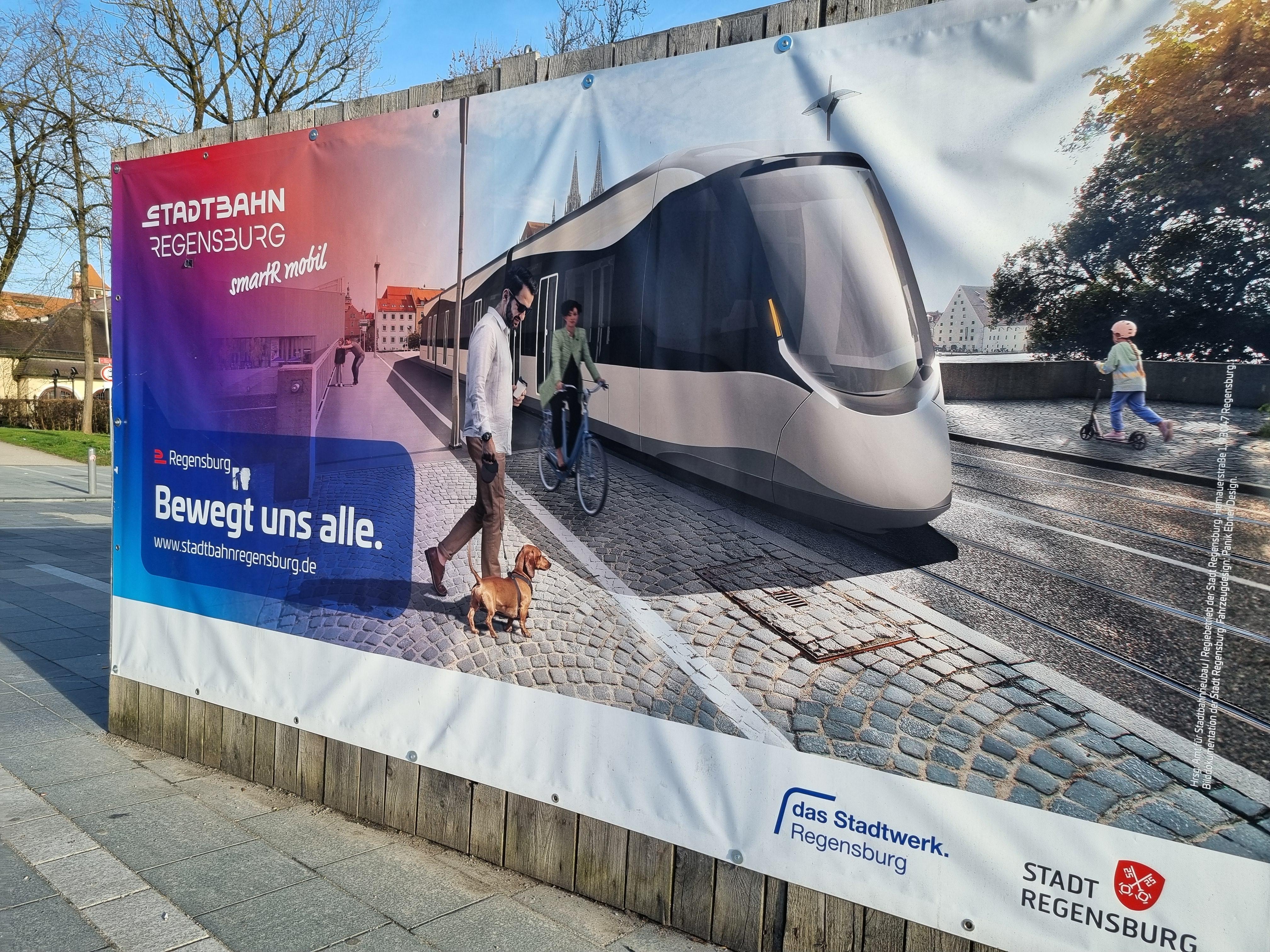 Eine Plakatwand zeigt wie die geplante Stadtbahn Regensburg aussehen könnte. 