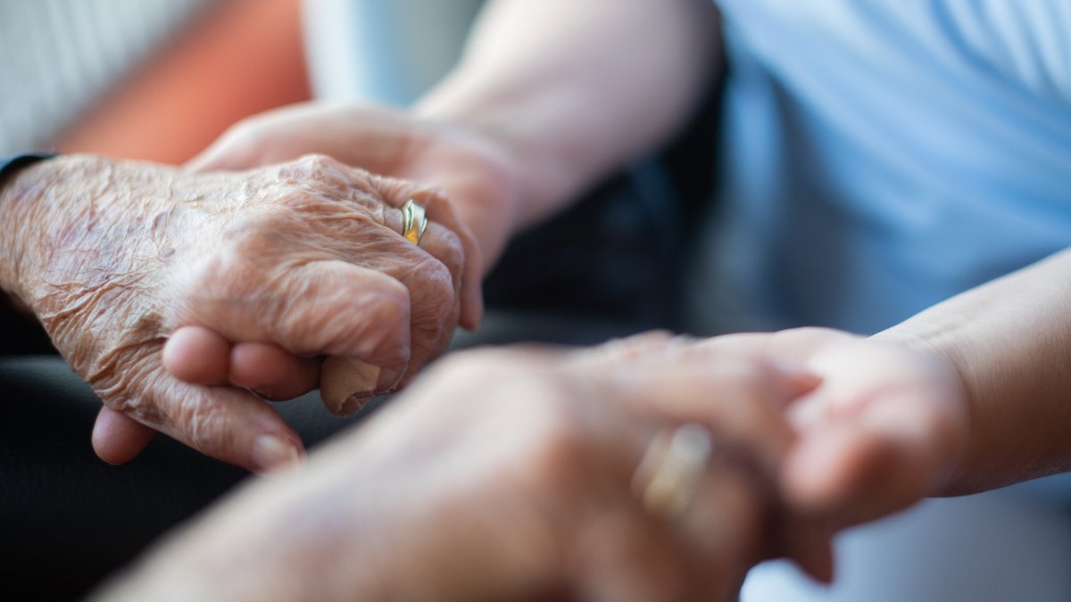 Eine Pflegerin hält in einem Pflegeheim die Hand einer Bewohnerin.