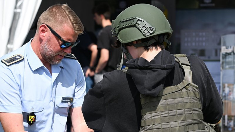 Ein Stabsfeldwebel der Bundeswehr legt einer jungen Frau eine schusssichere Weste an. (Archivbild) | Bild: dpa-Bildfunk/Arne Dedert Ein Stabsfeldwebel der Bundeswehr legt einer jungen Frau eine schusssichere Weste an. (Archivbild)