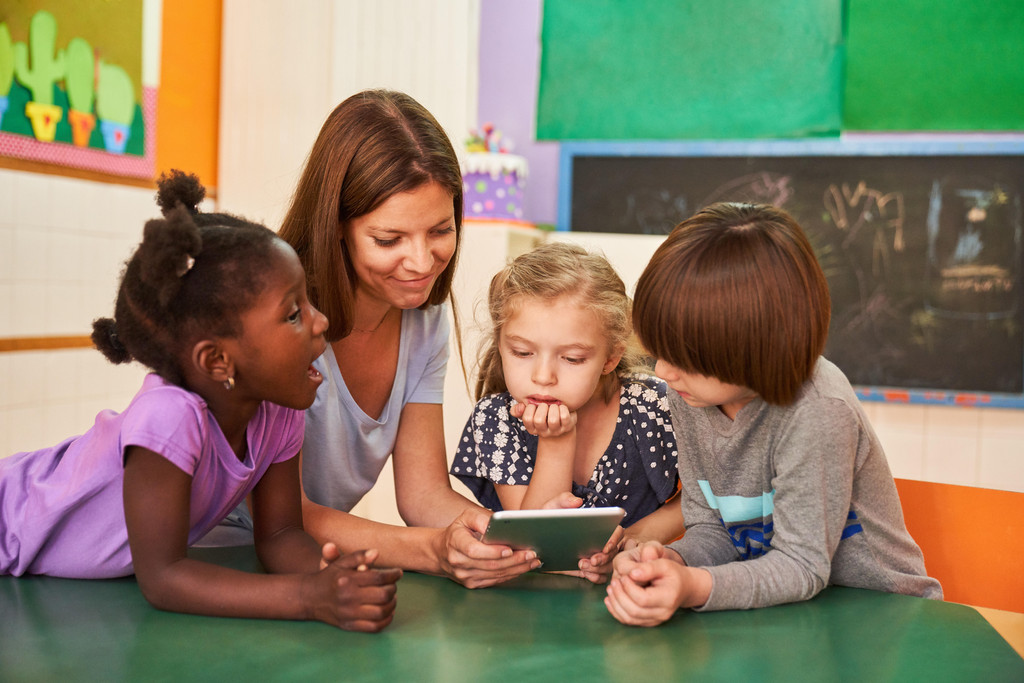 Erzieherin und Kinder mit Tablet Computer online im Kindergarten oder in der Vorschule