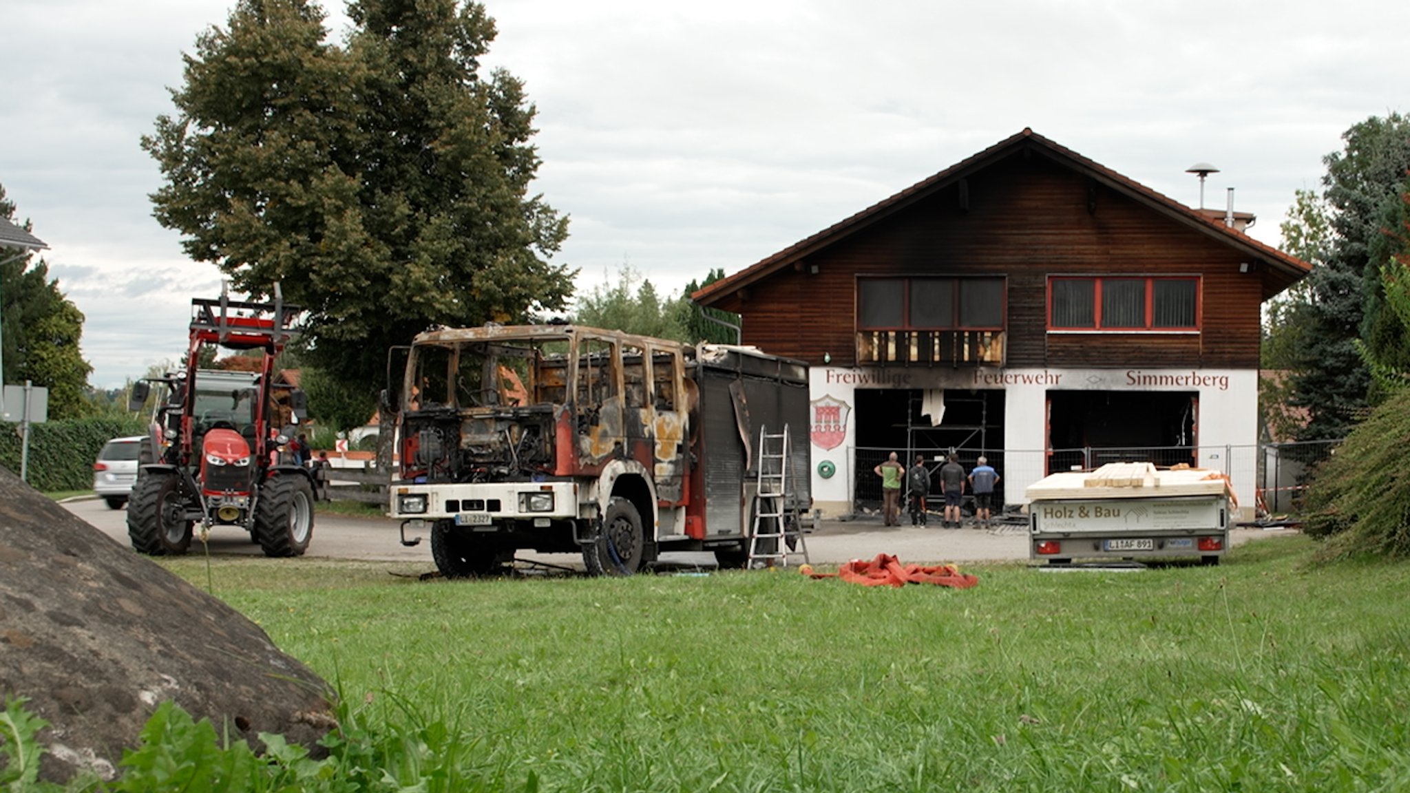 Das ausgebrannte Tanklöschfahrzeug steht vor dem rußschwarzen Gerätehaus der Freiwilligen Feuerwehr Simmerberg.