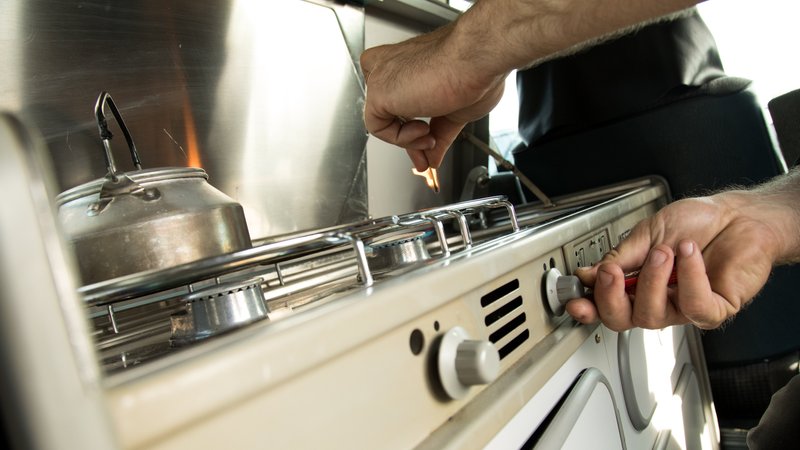 Ein Mann zuendet den Gasherd in einem Wohnmobil an (Symbolbild) | Bild: picture alliance / dpa-tmn | Christin Klose Ein Mann zuendet den Gasherd in einem Wohnmobil an (Symbolbild)
