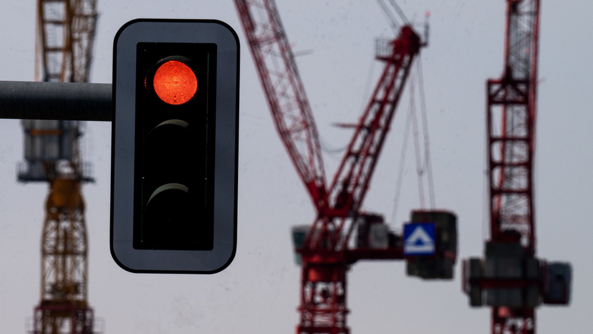 Auf einer Großbaustelle sind viele Kräne am Werk -  eine Ampel im Vordergrund zeigt rot.