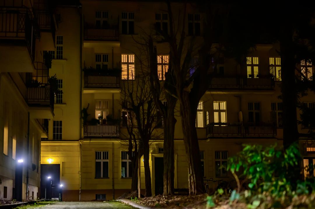 Blick auf das Hintergebäude einer Wohnanlage entlang eines beleuchteten Weges bei Nacht