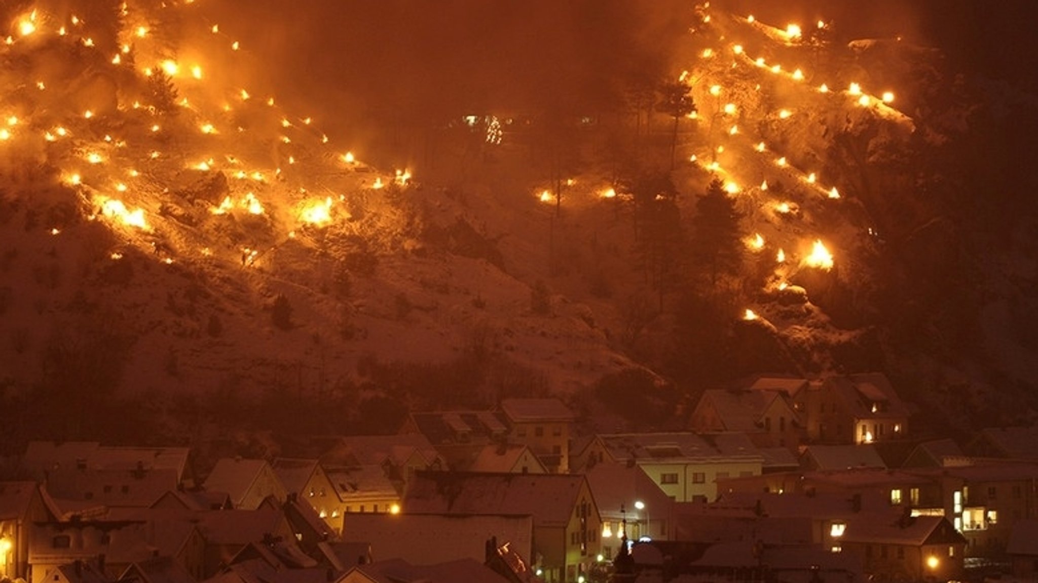 Blick auf Pottenstein und zahlreiche Bergfeuer im Schnee. 