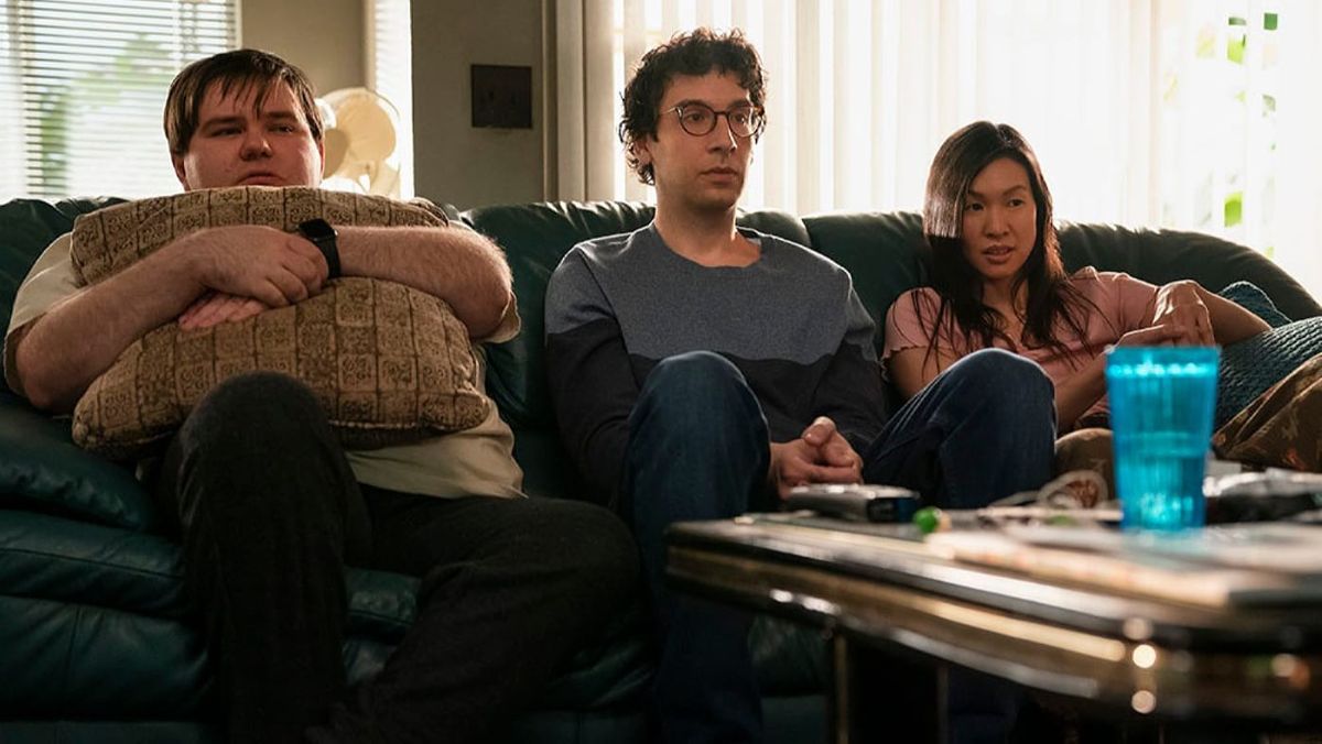 Man sieht drei junge Menschen auf einem Sofa sitzen - zwei Männer und eine Frau.