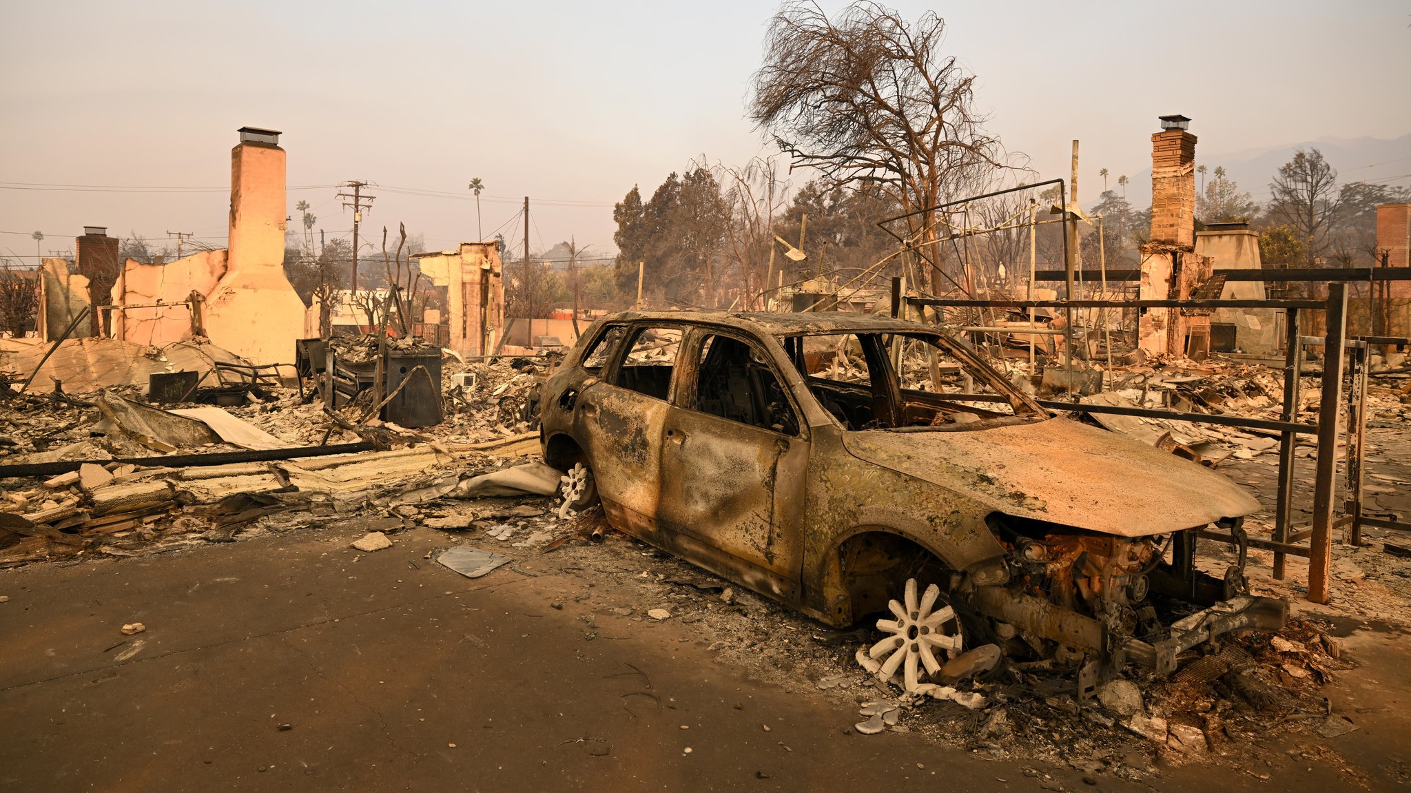 Ein ausgebranntes Fahrzeug und zerstörte Häuser in Los Angeles, aufgenommen am 9.1.25.