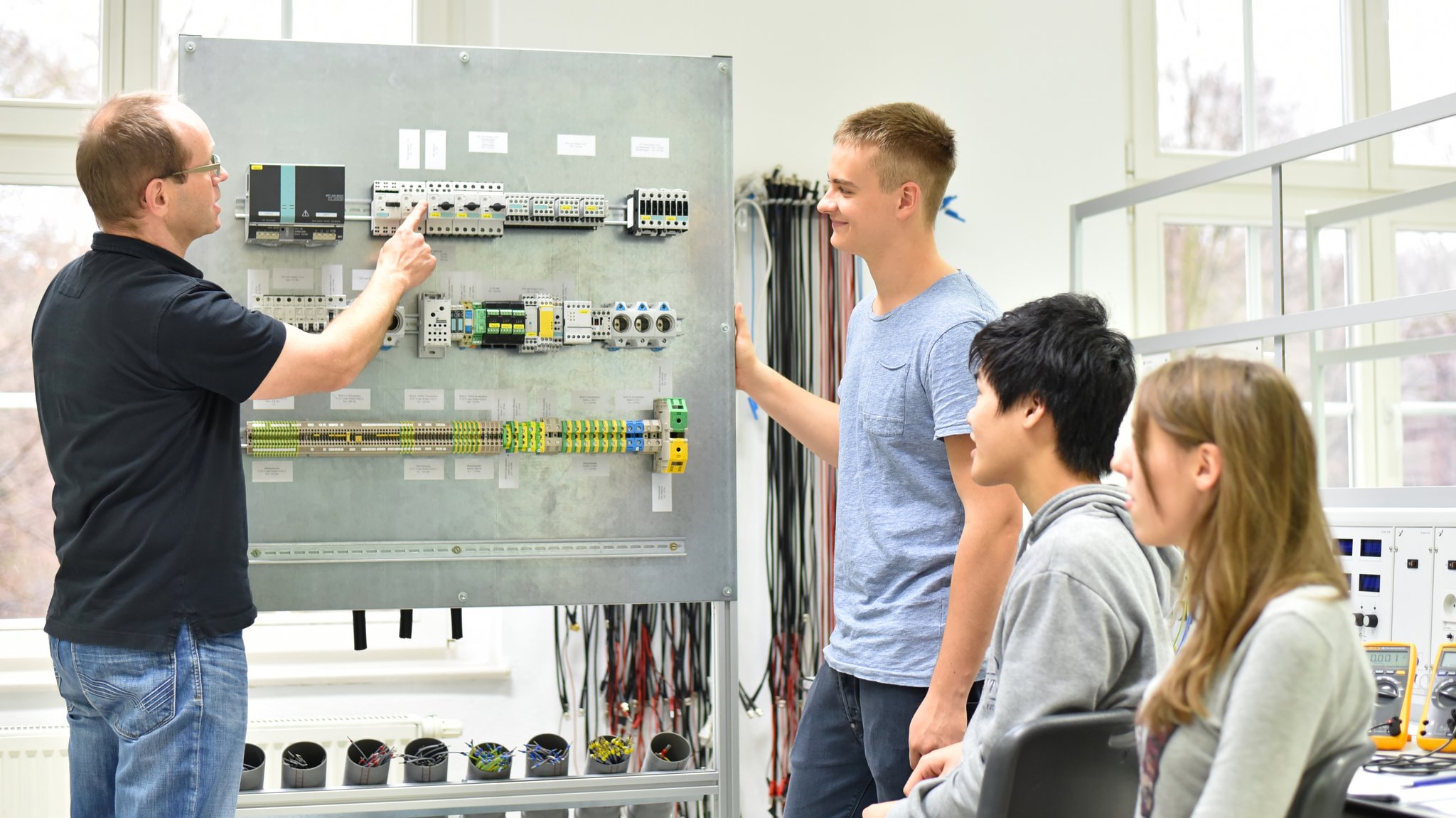 Ein Ausbilder erklärt jungen Menschen einen Schaltkasten mit Elektrotechnik. | Bild: stock.adobe.com/industrieblick Ein Ausbilder erklärt jungen Menschen einen Schaltkasten mit Elektrotechnik.