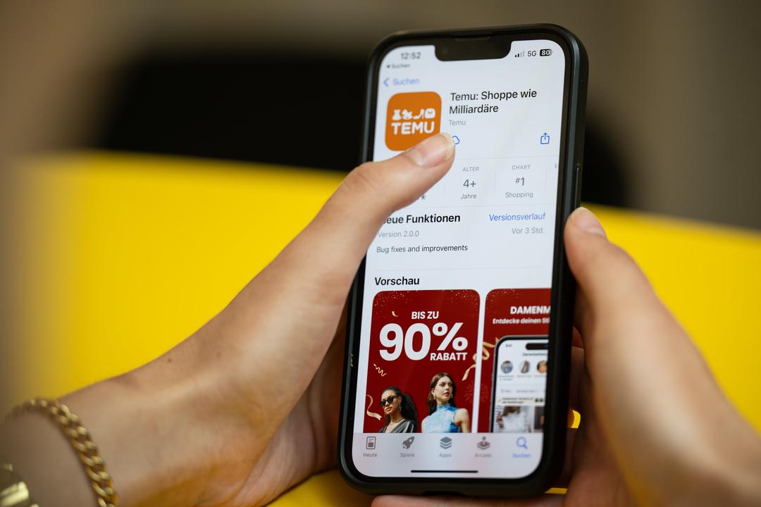 Eine Person hält ein Telefon mit der App Temu in den Händen. (Gestellte Szene).