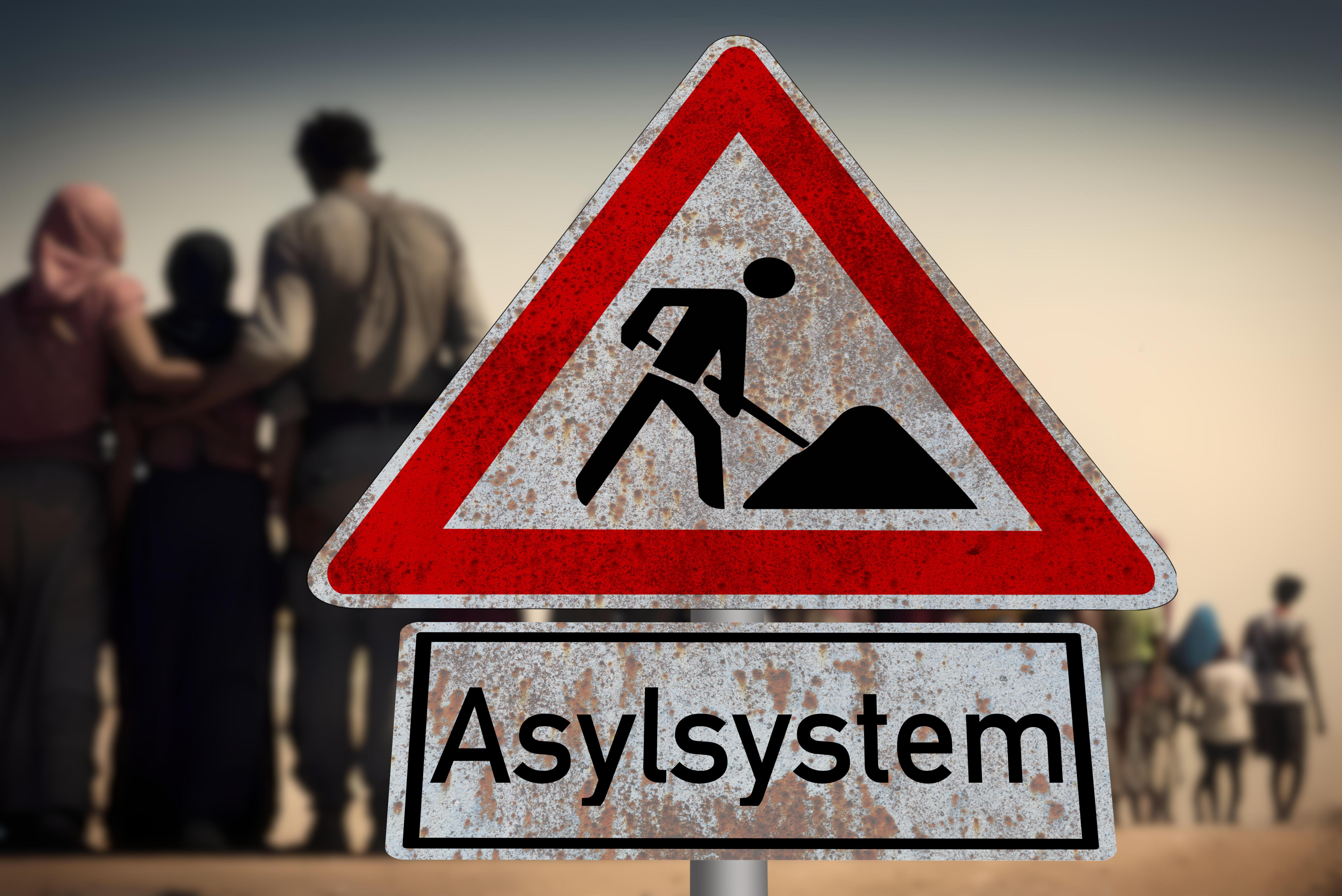 Ein Baustellensymbol mit der Aufschrift "Asylsystem" vor einer Familie.