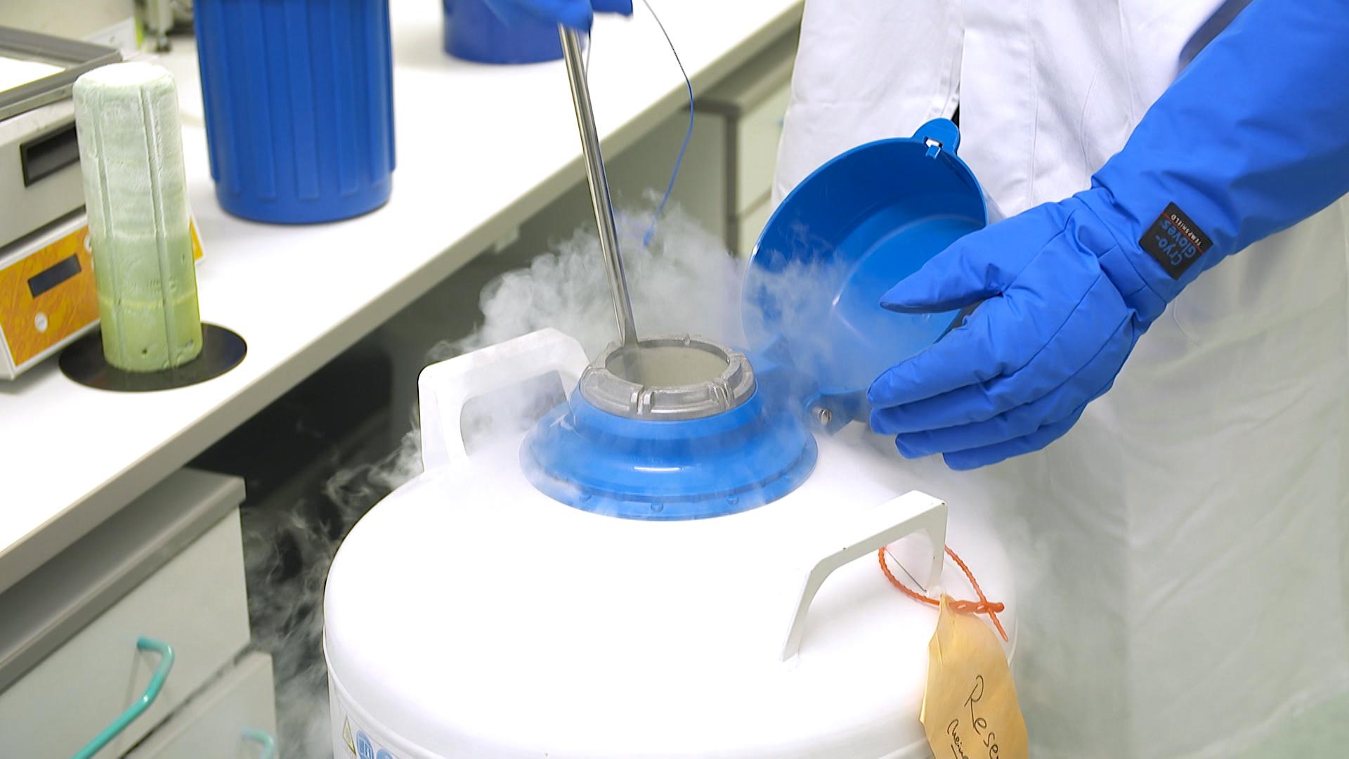 Aus einem weiß-blauen Kanister dampft es heraus. Hände in blauen Handschuhen führen einen Stab in die Öffnung ein.