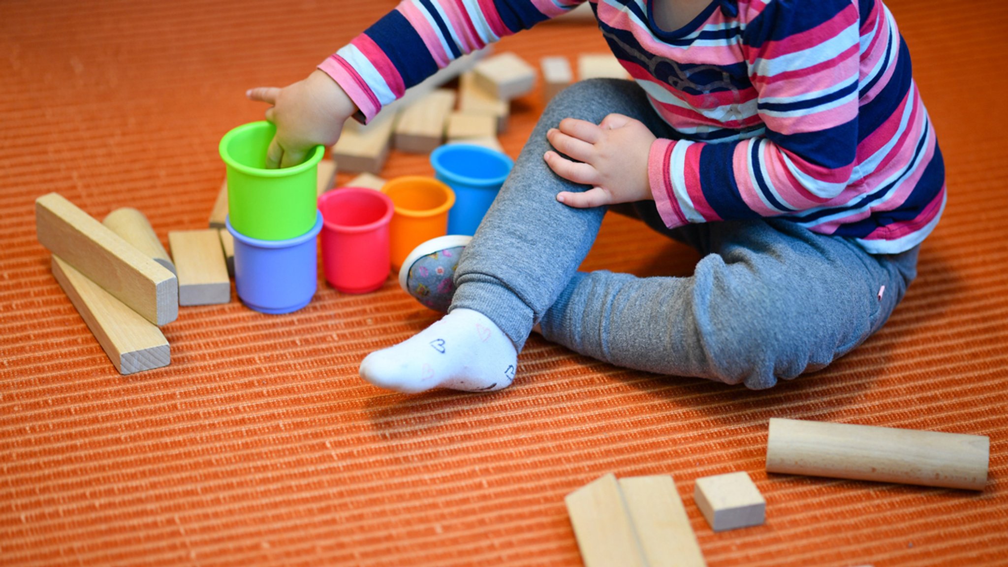 Ein Mädchen spielt in einer Kita mit bunten Bechern und Bauklötzen.