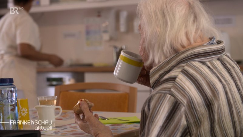 Eine ältere Frau trinkt aus einer Tasse.