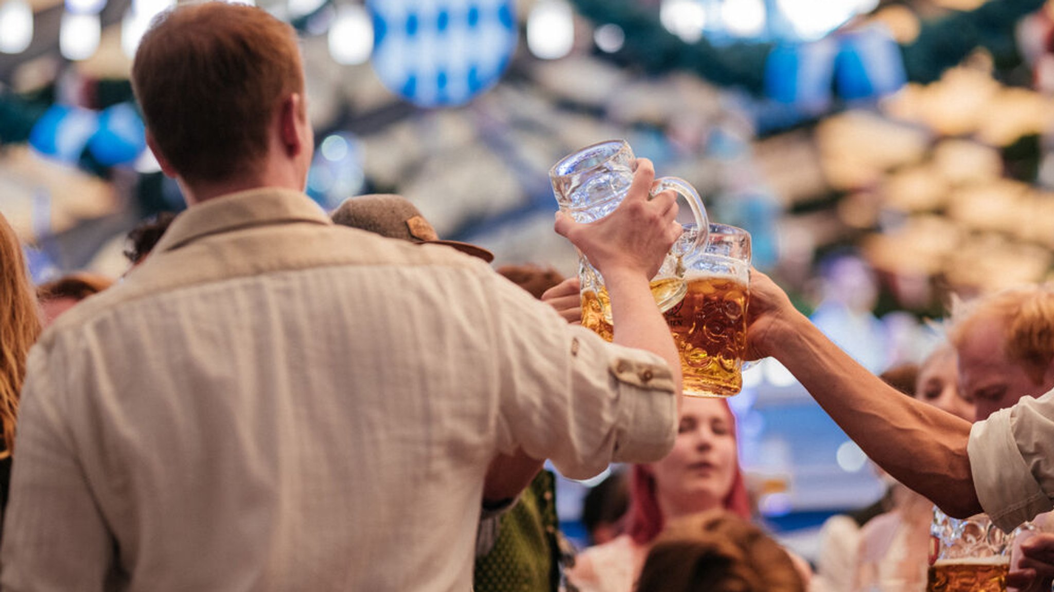 Männer stoßen auf der Wiesn mit einer Maß Bier zusammen an.