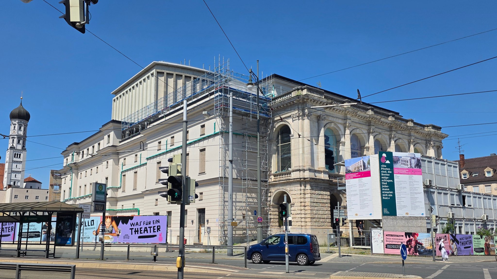 Das Staatstheater Augsburg mit Gerüst, davor ein Plakat mit der Aufschrift "Was für ein Theater".