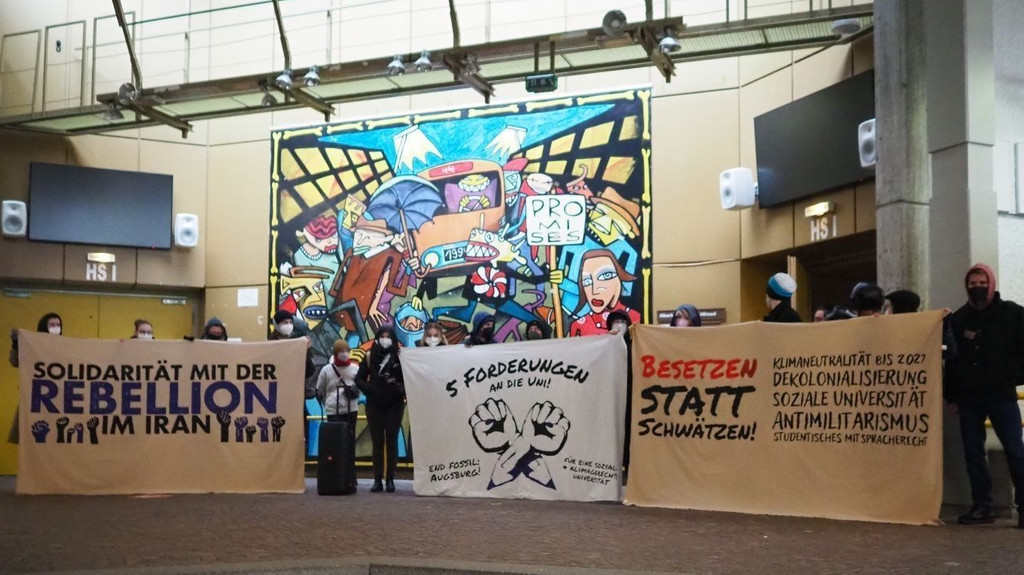 Klima-Aktivisten stehen am 28.11.2022 mit Plakaten vor dem großen Hörsaal der Universität Augsburg