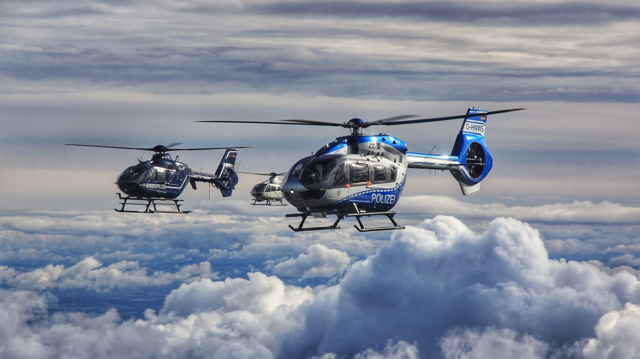 Polizeihubschrauber im Formationsflug über Wolken