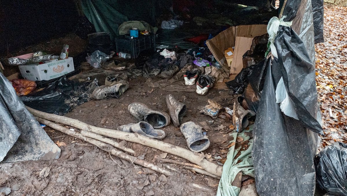 Schuhe und andere Gegenstände liegen in einem unbefestigten Zelt im Matsch.