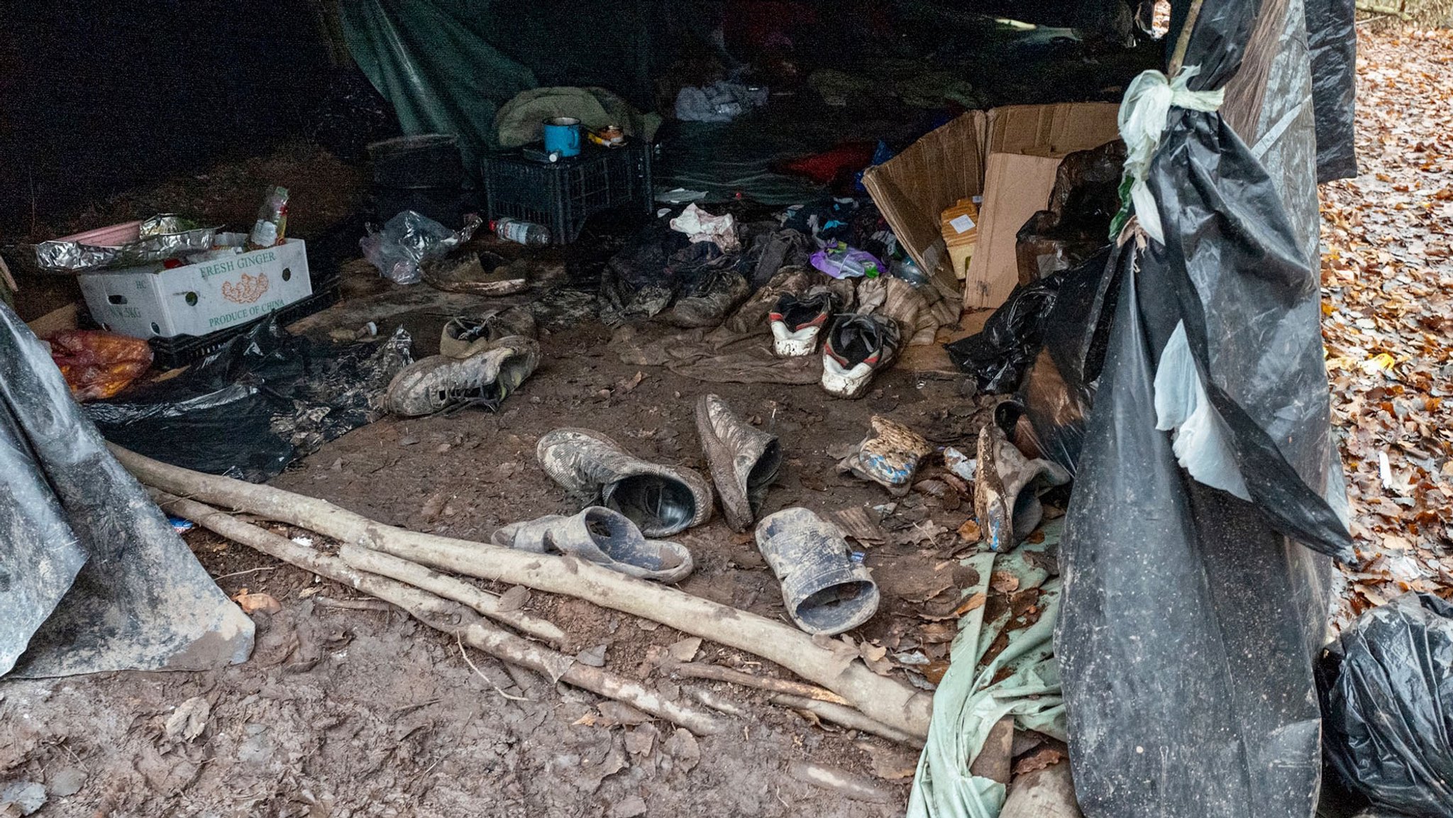 Schuhe und andere Gegenstände liegen in einem unbefestigten Zelt im Matsch.