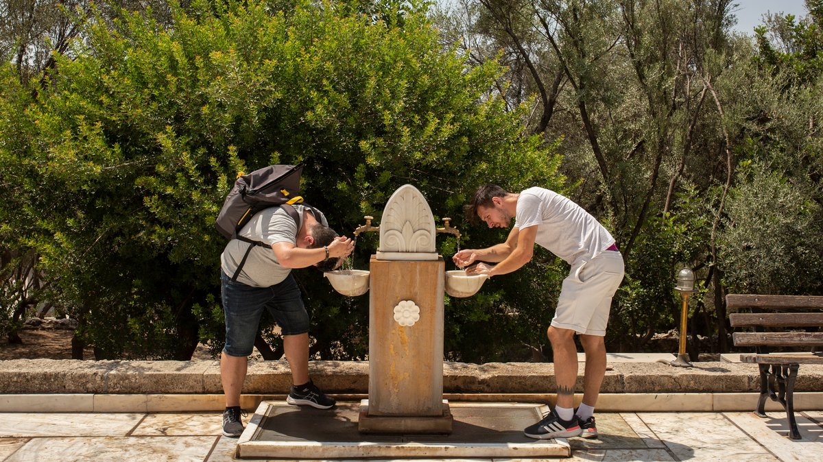Touristen erfrischen sich während ihres Besuchs auf der Akropolis im Zentrum Athens an einem öffentlichen Trinkbrunnen. (Archivbild vom 21.7.23)
