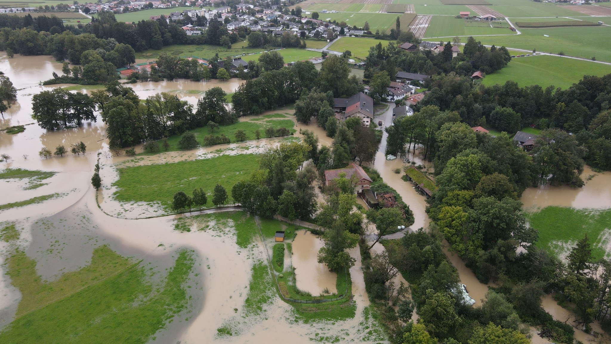 Luftaufnahme des Ortes Oberkaltenbrunn im Landkreis Rosenheim: Straßen und Felder sind mit braunem Wasser überschwemmt.