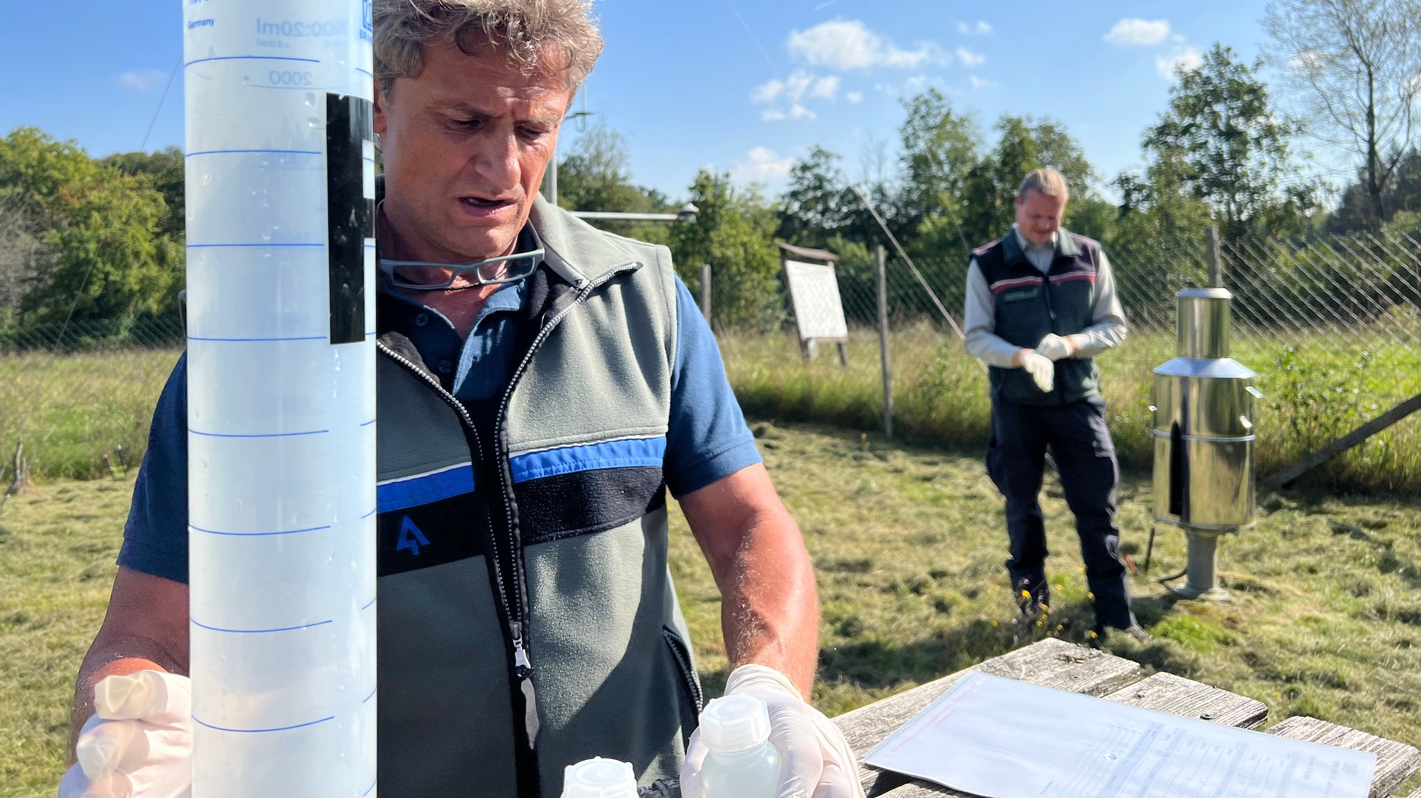 Forstwirt Stephan Hanke ist in einem eingezäunten Bereich beschäftigt und füllt Wasser aus Auffangbehältern ab. 