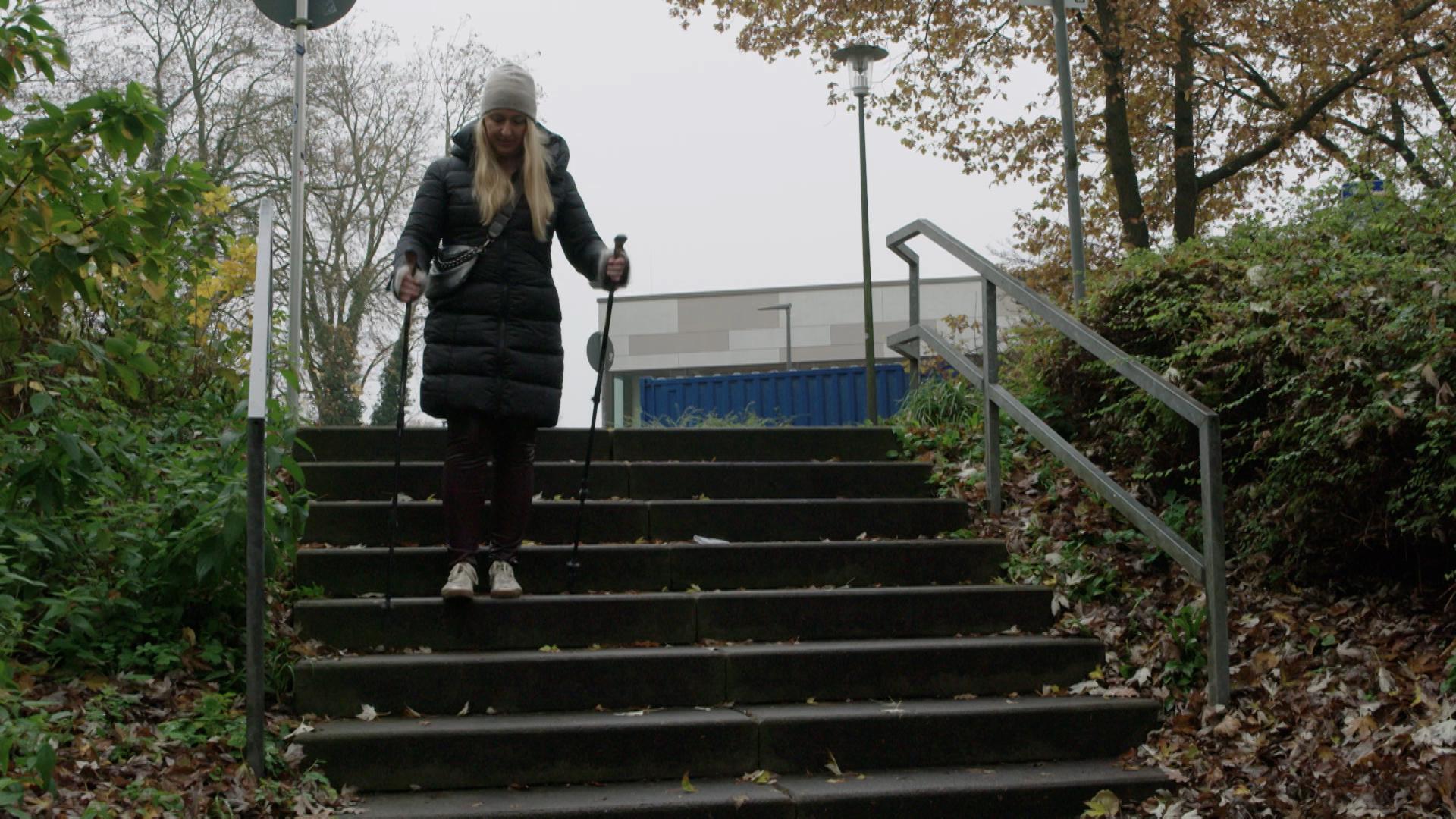 Eine blonde Frau geht mit Gehstöcken eine Treppe hinunter.