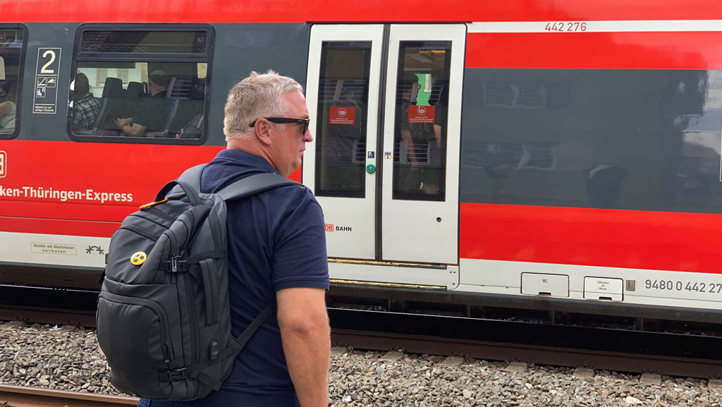 Ein Mann mit Rucksack schaut einem vollen Zug hinterher.
