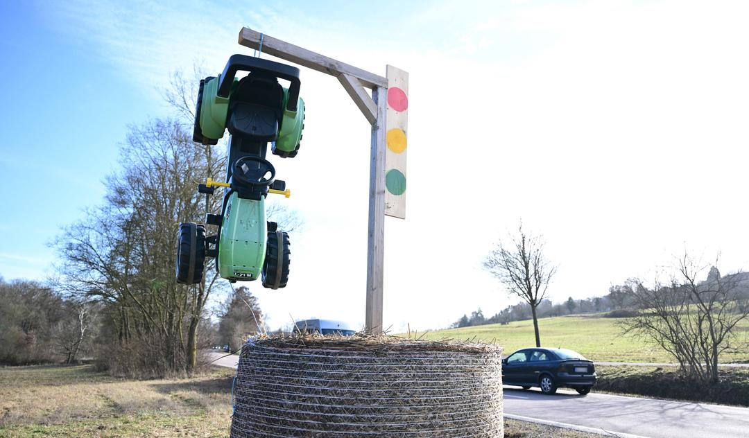 Zu sehen ist ein Spielzeugtraktor, der an einem Holzgalgen aufgehangen ist. Auf dem Holzpfosten ist eine Ampel angebracht.