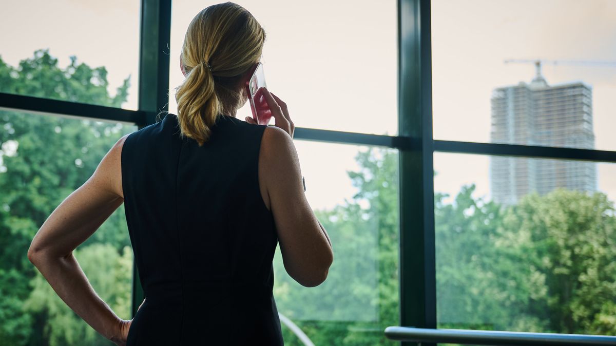 Eine Frau steht in einem Bürozimmer am Fenster und telefoniert (Symbolbild)