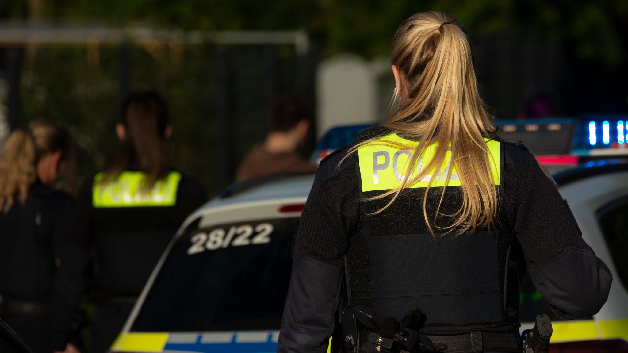 Ein Beamtin der Polizei steht an einem Streifenwagen mit Blaulicht (Symbolbild).