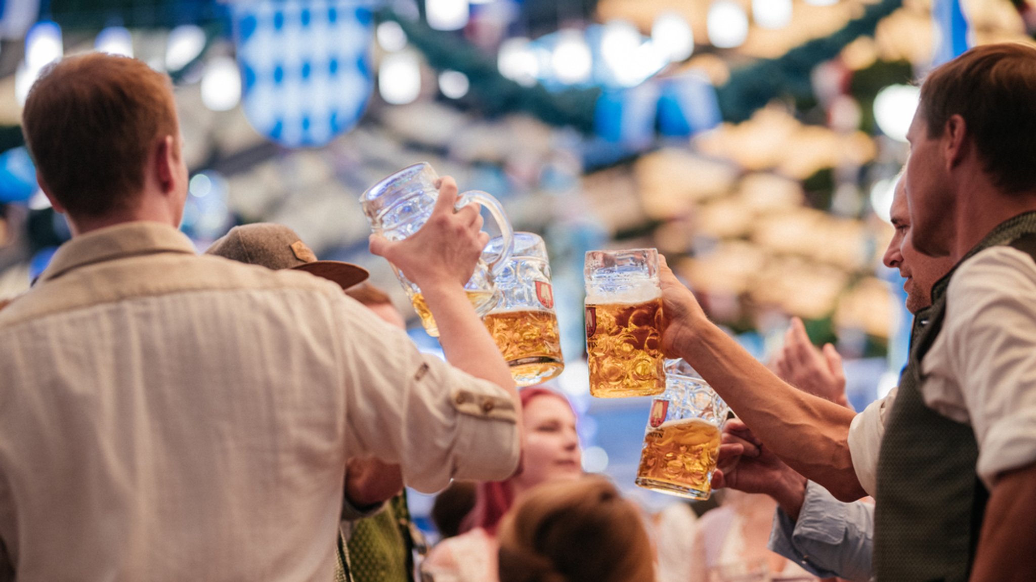 Männer stoßen auf der Wiesn mit einer Maß Bier zusammen an ((Symbol- und Archivbild)