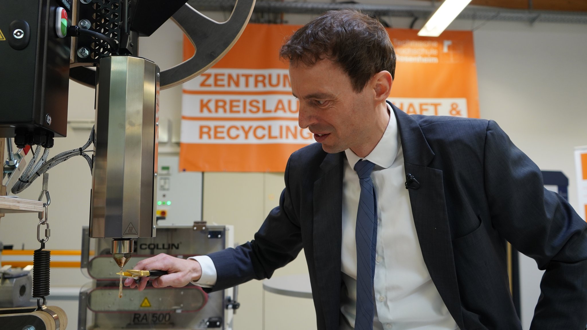 Zu sehen ist Johannes Eben, wie er vor einer manuellen Maschine steht, die Kunststoff erhitzen und in neue Formen spritzen kann. | Bild: BR/Alisa Schröter Zu sehen ist Johannes Eben, wie er vor einer manuellen Maschine steht, die Kunststoff erhitzen und in neue Formen spritzen kann.