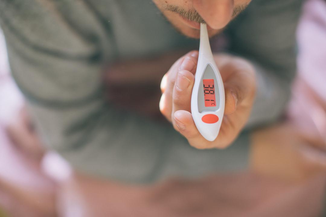 Eine Person misst ihre Temperatur mit einem Fieberthermometer.