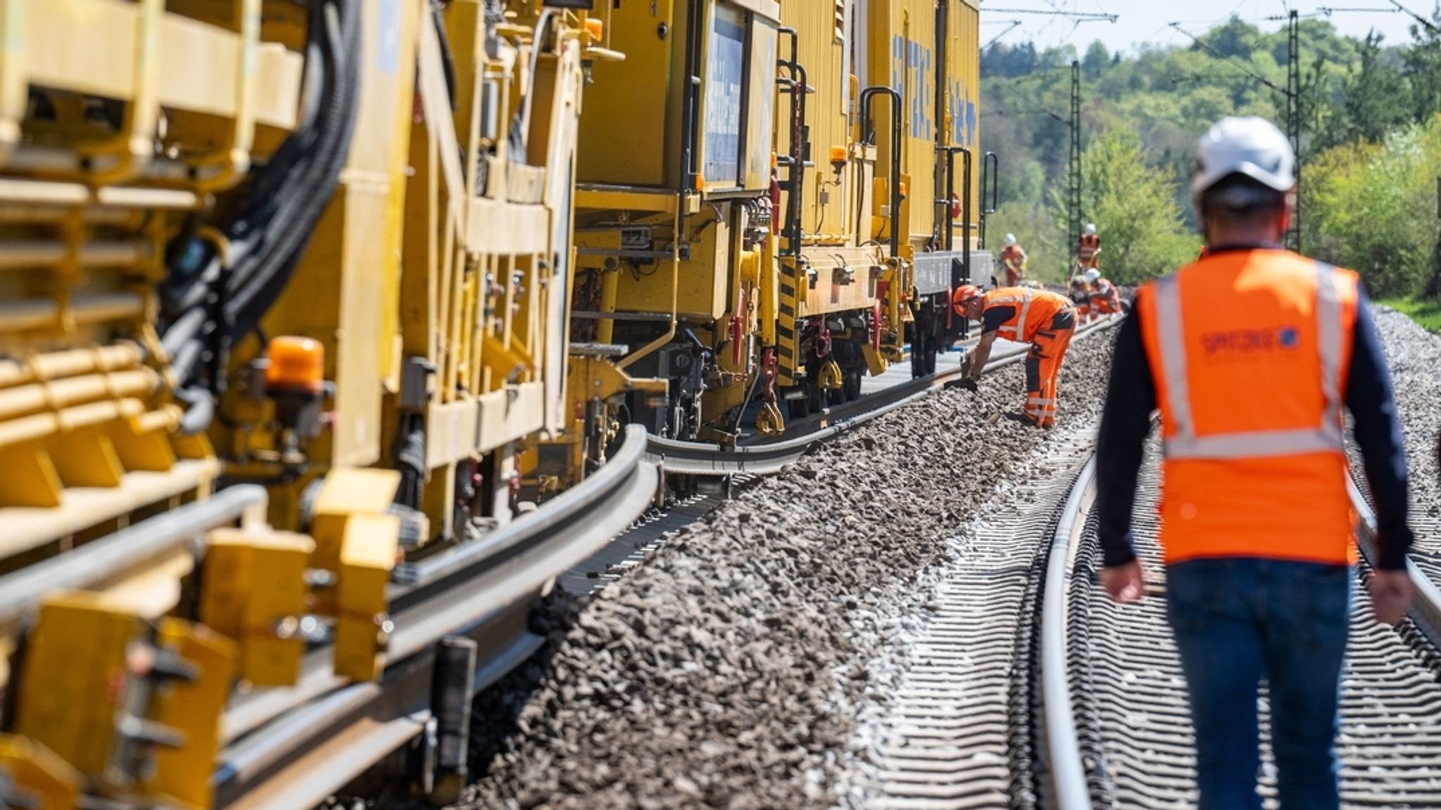 Bauarbeiter und Maschinen an Bahnstrecke. 