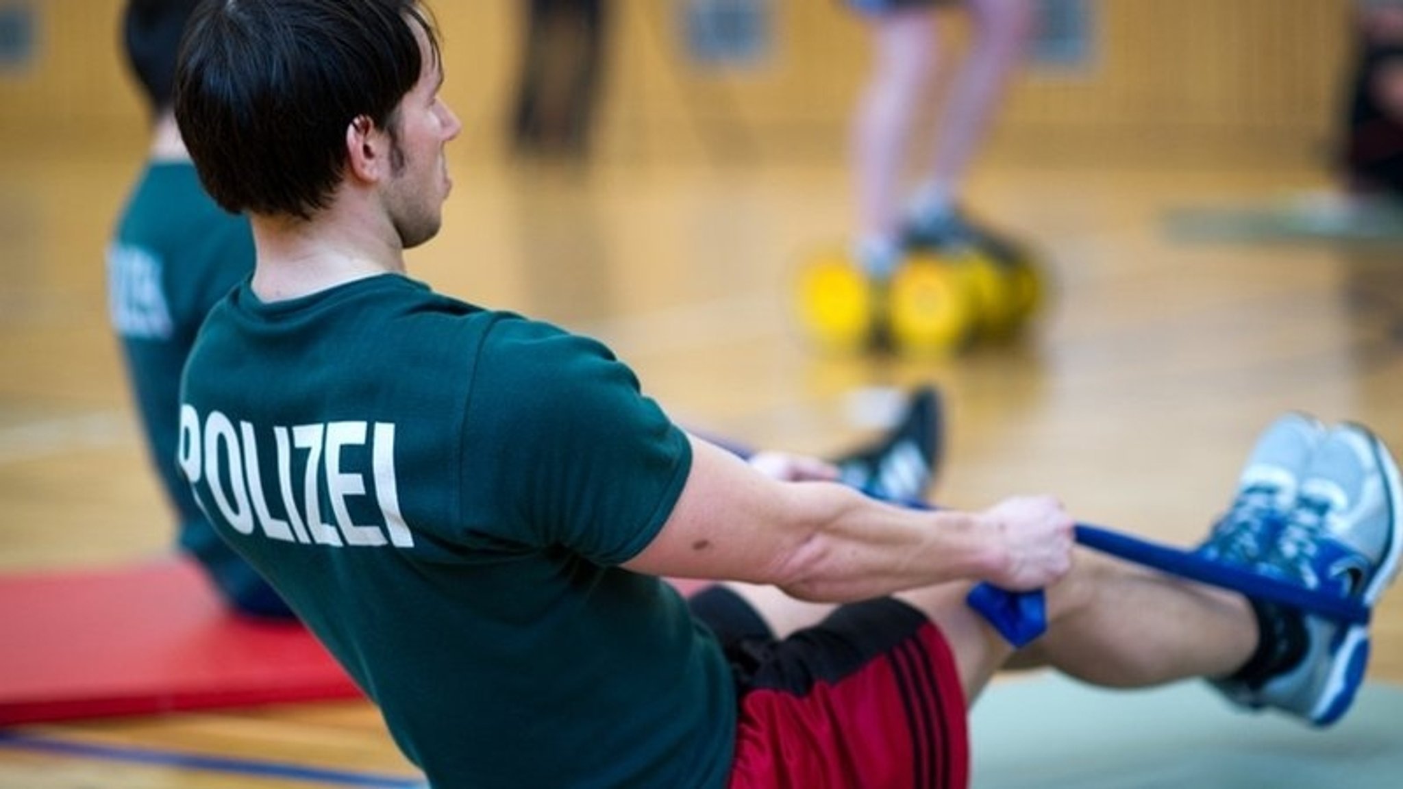 Ein Mann trainiert in einer Turnhalle mit einem Theraband. 