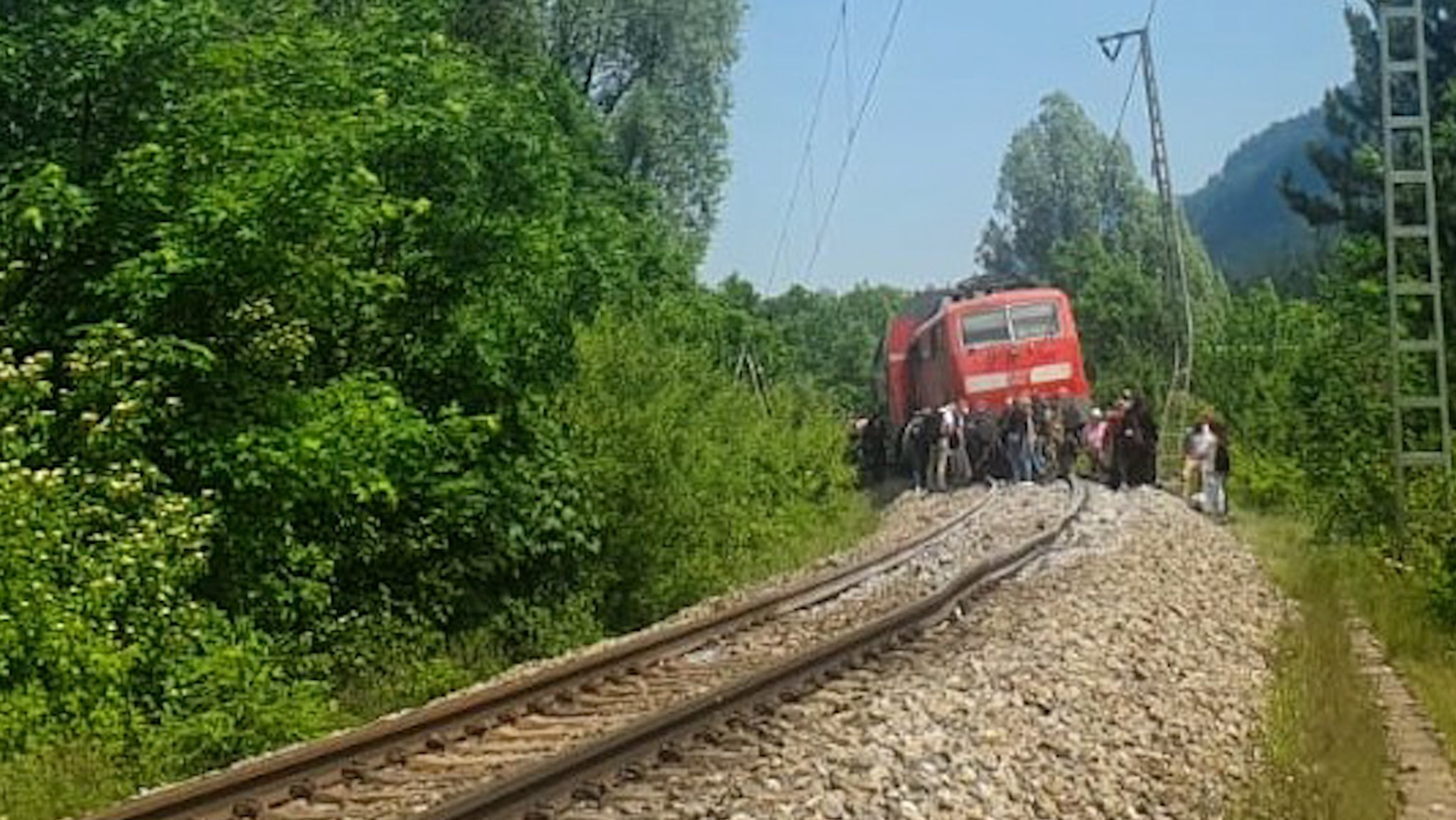 Menschen vor einem Zug auf einer eingleisigen Bahnstrecke