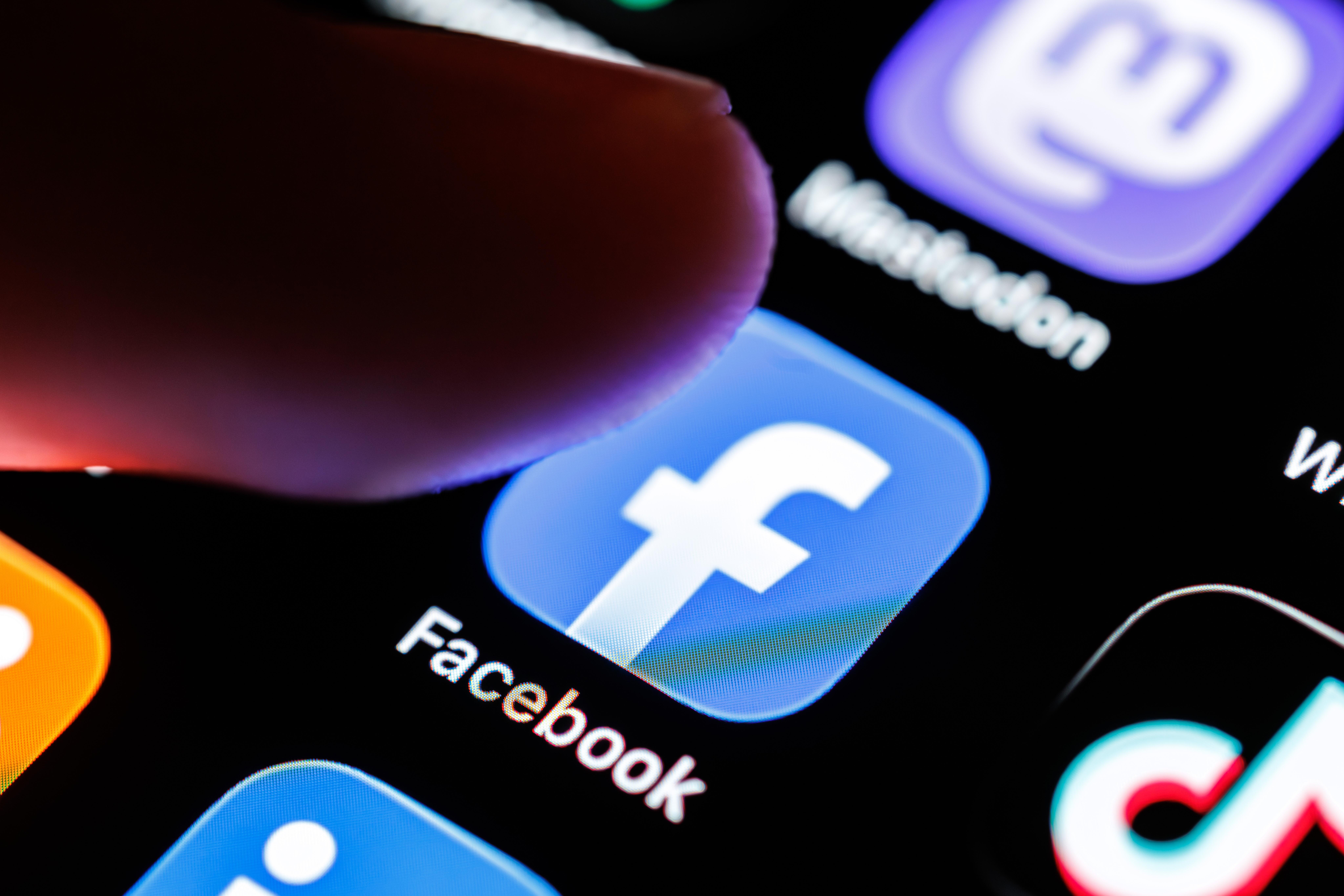 Das Logo der App Facebook ist auf dem Display von einem Smartphone zu sehen, während ein Finger auf das Symbol der Applikation tippt. 