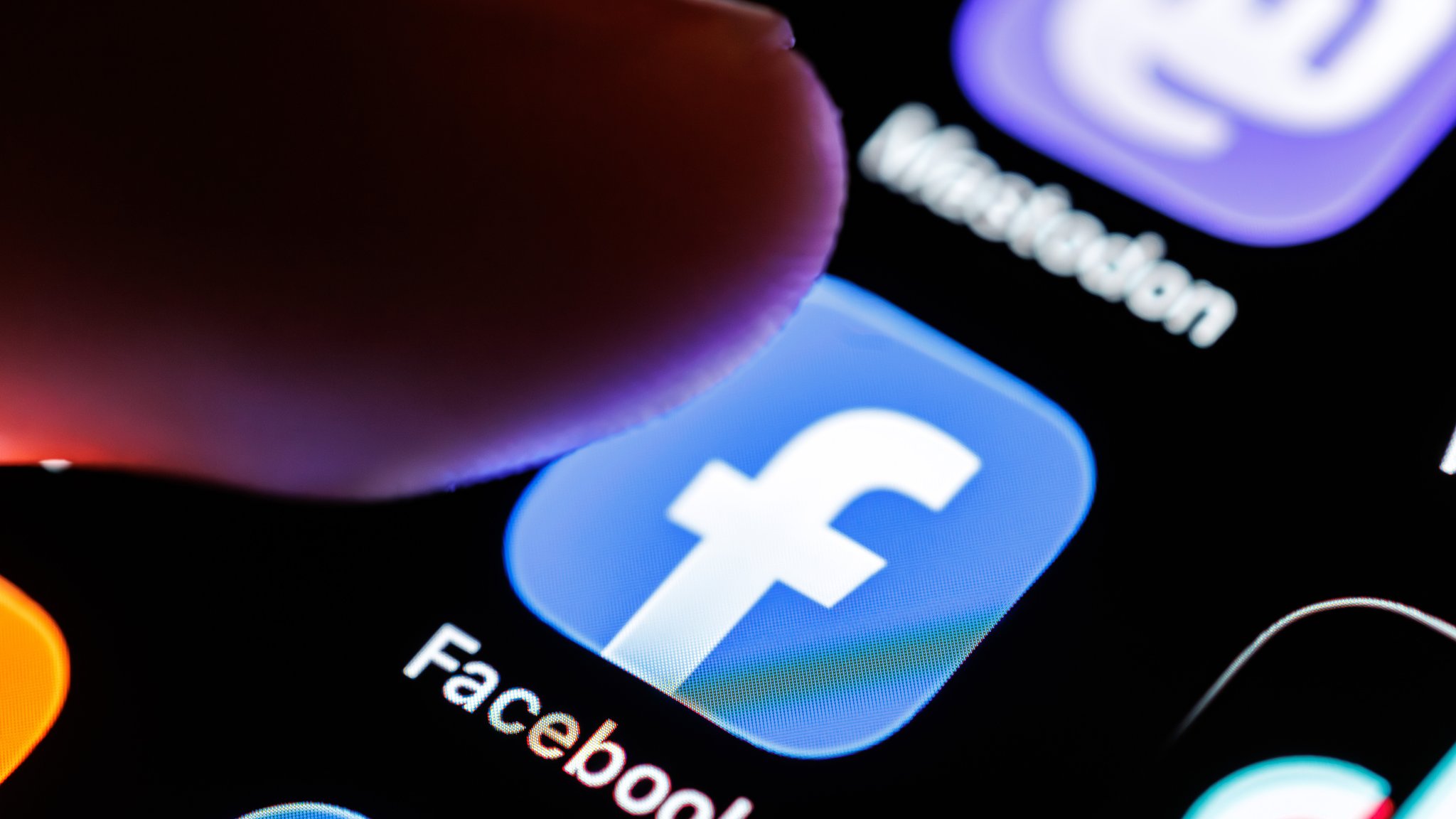 Das Logo der App Facebook ist auf dem Display von einem Smartphone zu sehen, während ein Finger auf das Symbol der Applikation tippt. 