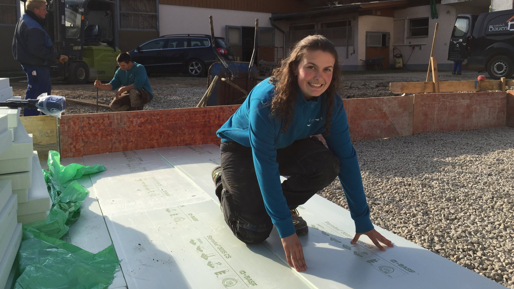 Eine junge Frau kniet auf einer Baustelle.