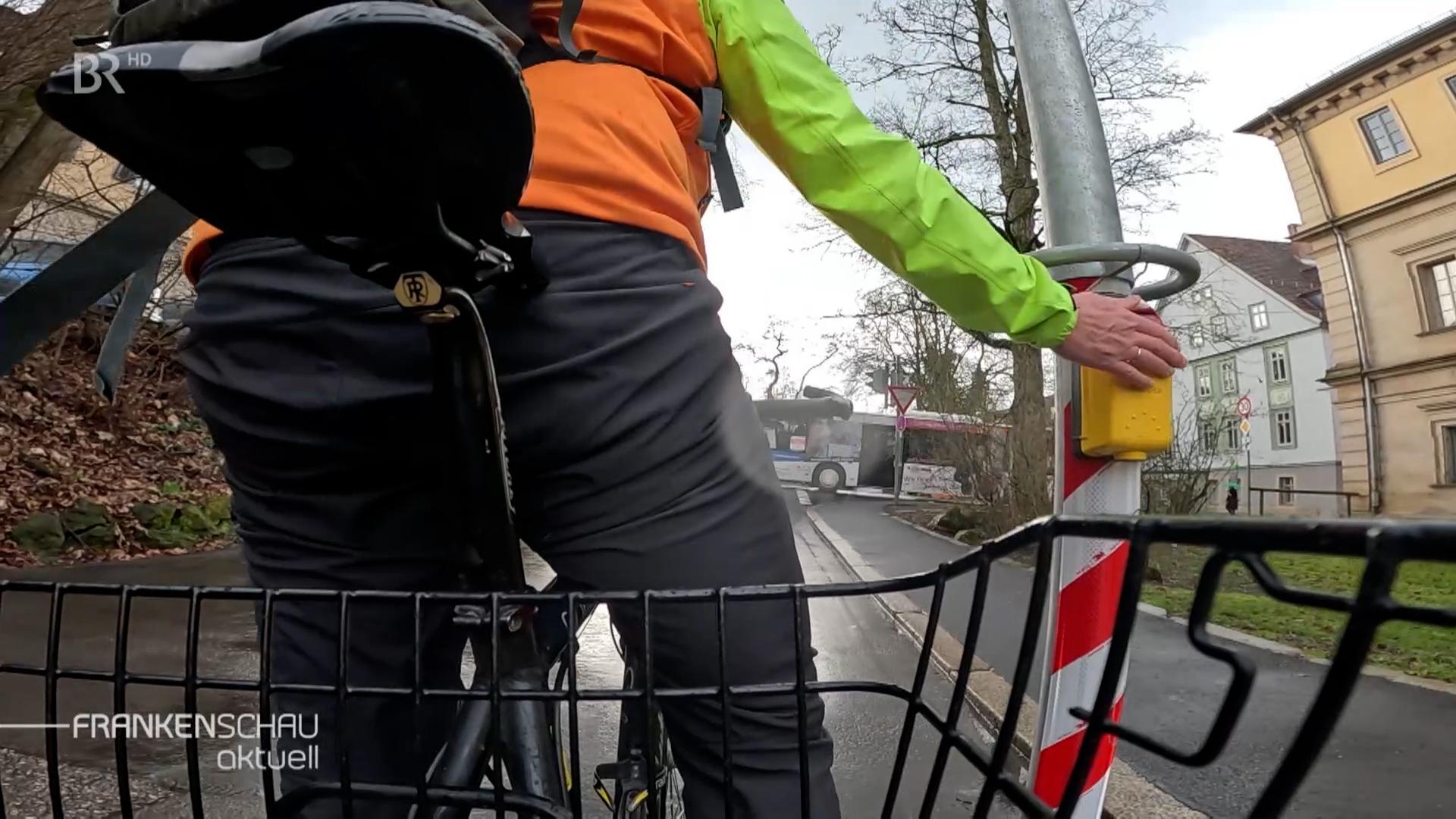 Ein Fahrradfahrer drückt einen Ampeldrückknopf. 