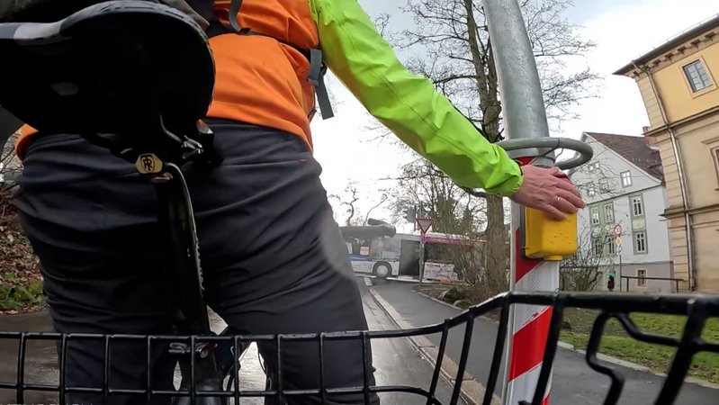 Ein Fahrradfahrer drückt einen Ampeldrückknopf. 