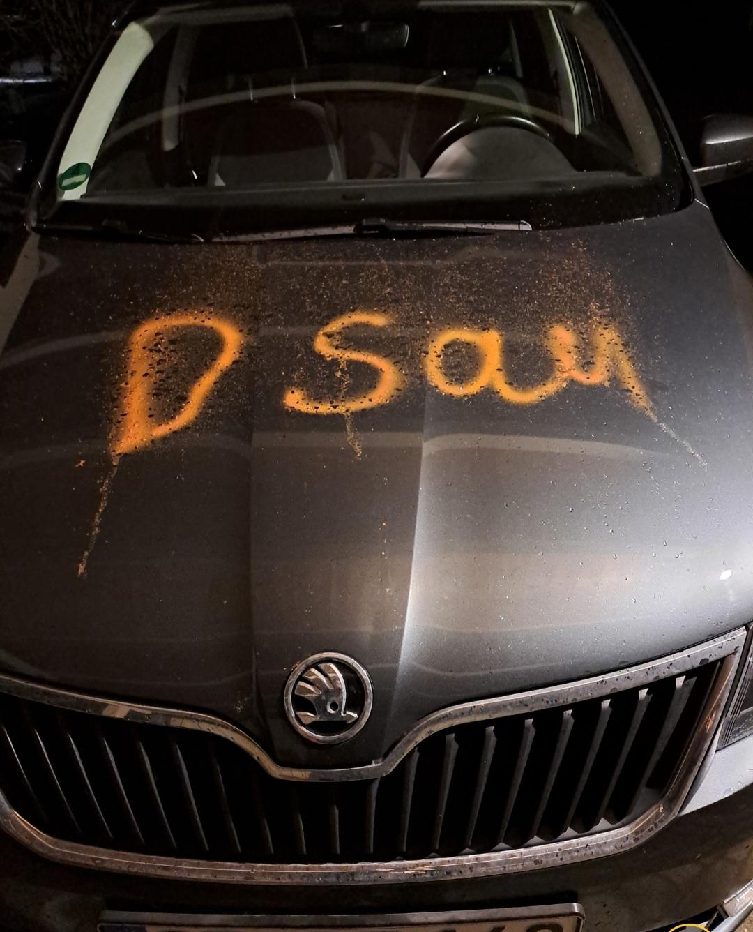 Schwarzes Auto mit der orangefarbenen Aufschrift "Sau". 