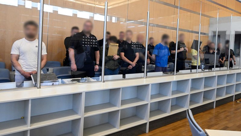30.07.2024, Nordrhein-Westfalen, Düsseldorf: Insgesamt sieben Angeklagte stehen zum Prozessbeginn des Staatsschutzverfahren gegen sieben mutmassliche Gründer und Mitglieder einer inländischen terroristischen Vereinigung im Oberlandesgericht an der Anklagebank. Die Männer sollen den Überfall Russlands auf die Ukraine genutzt haben, um über die Ukraine nach Deutschland zu gelangen. In Deutschland angekommen sollen sie eine Terrorzelle des IS gegründet und Geld für die Organisation gesammelt haben. Foto: Roberto Pfeil/dpa - ACHTUNG: Angeklagte und Justizbeamte wurden auf Anweisung des Gerichts aus rechtlichen Gründen gepixelt +++ dpa-Bildfunk +++ | Bild: dpa-Bildfunk/Roberto Pfeil 30.07.2024, Nordrhein-Westfalen, Düsseldorf: Insgesamt sieben Angeklagte stehen zum Prozessbeginn des Staatsschutzverfahren gegen sieben mutmassliche Gründer und Mitglieder einer inländischen terroristischen Vereinigung im Oberlandesgericht an der Anklagebank. Die Männer sollen den Überfall Russlands auf die Ukraine genutzt haben, um über die Ukraine nach Deutschland zu gelangen. In Deutschland angekommen sollen sie eine Terrorzelle des IS gegründet und Geld für die Organisation gesammelt haben. Foto: Roberto Pfeil/dpa - ACHTUNG: Angeklagte und Justizbeamte wurden auf Anweisung des Gerichts aus rechtlichen Gründen gepixelt +++ dpa-Bildfunk +++