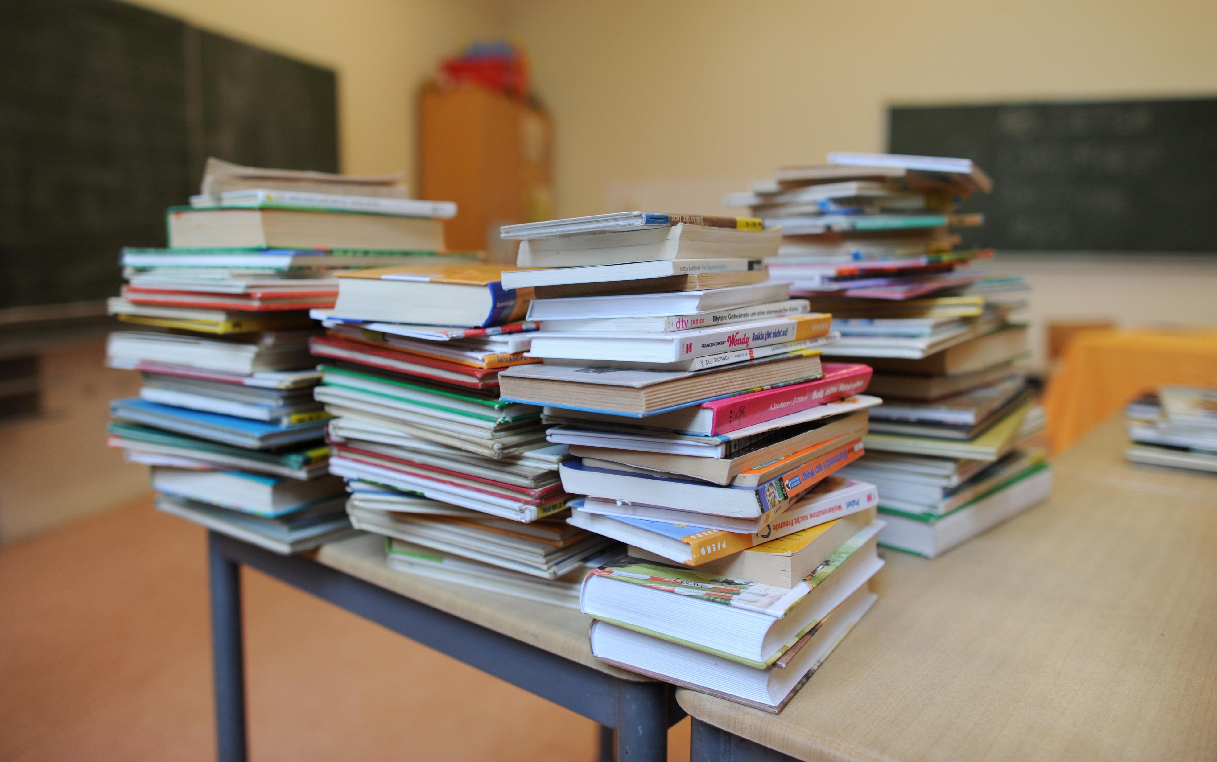 Bücher stapeln sich auf einem Tisch in einem Klassenzimmer.